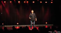 Mann im schwarzen Hemd auf rot beleuchteter Bühne vor Silhouette des Publikums, Quelle: DTF