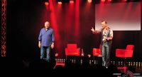 zwei Männer auf der rot beleuchteten Bühne vor Silhouette des Publikums, Quelle: DTF