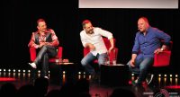 drei sitzende Männer in roten Stühlen vor Silhouette des Publikums, Quelle: DTF