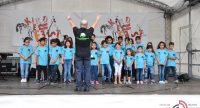 Kinderchor in türkisen Shirts vor Chorleiter mit erhobenen Händen mit schwarzem T-Shirt, Quelle: DTF