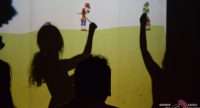 sitzende Erwachsene schauen in Richtung Schattentheater zweier Mädchen, Quelle: DTF