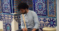 Mann im blauen Hemd spielt Kaval sitzend vor blauer Arabeske, Quelle: DTF