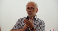 Mann im weiß schwarzen Hemd spricht ins Mikrofon, die linke Hand vor sich erhoben, Quelle: DTF