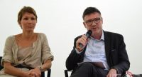 Mann und Frau sitzend, der Mann im schwarzen Anzug spricht Richtung Publikum, Quelle: DTF