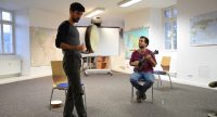 ein stehender Mann spricht gestikulierend, ein sitzender Musiker schaut ihm zu, Quelle: DTF