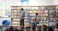 zwei junge Männer und ein Mädchen vor sitzendem Publikum, Quelle: DTF