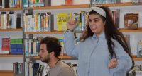 junger Mann sitzend und Mädchen stehend vor einem Bücherregal, Quelle: DTF
