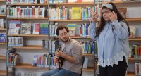 junger Mann sitzend und Mädchen stehend vor einem Bücherregal, Quelle: DTF