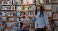 junger Mann sitzend und Mädchen stehend vor einem Bücherregal, Quelle: DTF