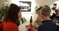Menschen stehend rund um einen Tisch unterhalten sich mit Weingläsern in drn Händen, Quelle: DTF
