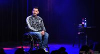 Mann im Rollstuhl und Tarnfarben Oberteil spricht Richtung Publikum, Quelle: DTF