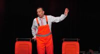 Mann im grauen Hemd mit orangenem Overall steht neben zwei geöffneten Mülltonnen, Quelle: DTF