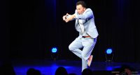 Mann im hellblauen Anzug tanzend auf der Bühne vor Silhouette des Publikums, Quelle: DTF