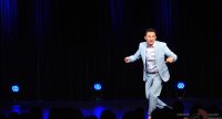Mann im hellblauen Anzug rennt über die Bühne vor Silhouette des Publikums, Quelle: DTF