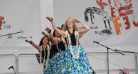 Frauen in traditioneller Kleidung tanzend auf der Bühne mit Banner des Kinderfests, Quelle: DTF