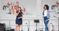 zwei Frauen sprechend auf der Bühne mit Banner des Kinderfests, Quelle: DTF