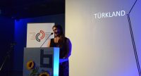 Seyhan Caliskan Turan lächelnd am Rednerpult vor Banner des DTF, Quelle: DTF