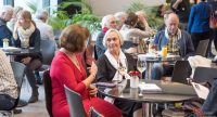 Menschen sitzen an runden Tischen mit Getränken und unterhalten sich, Quelle: DTF