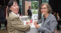 zwei Damen im Sakko mit Weingläsern in der Hand schauen freundlich in die Kamera, Quelle: DTF