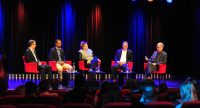Fünf Diskussionteilnehmer sitzend auf roten Stühlen vor schwarzem Vorhand und Silhouette des Publikums im Bildvordergrund, Quelle: DTF
