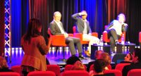 zwei Männer und eine Frau sitzend auf roten STühlen schauen auf eine Frau im Publikum, welche eine Frage stellt, Quelle: DTF