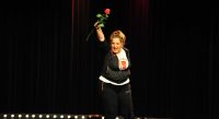 Frau in schwarzem Kapuzenpulli hält froh eine Rose mit der rechten Hand hoch, Quelle: DTF