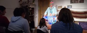 Frau im türkisen Mantel mit Kopftuch steht am Puppentheater