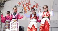 traditionell angezogene Mädchen tanzend auf der Bühne mit Banner vom Kinderfest im Hintergrund, Quelle: DTF