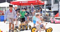 Kinder auf Holzfahrzeugen mit gelben Rädern, Quelle: DTF