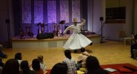 Tänzer in traditioneller Kleidung vor auf dem Boden hockenden Kindern, Quelle: DTF
