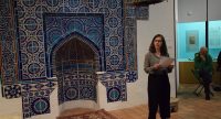 Frau liest von einem Blatt ab während sie vor einer blau gefliesten Arabeske steht, Quelle: DTF