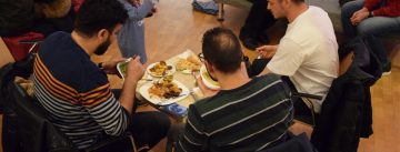 vier Menschen sitzend rund um einen Tisch essen gut beladene Teller