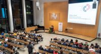 Saal mit SItzreihen, Podium und weißer Leinwand von oben fotografiert, Quelle: DTF