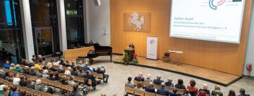 Saal mit SItzreihen, Podium und weißer Leinwand von oben fotografiert