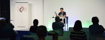 Hasnain Kazim sitzend auf dem Podium vor Silhouette des Publikums
