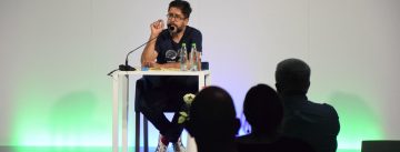 Hasnain Kazim sitzend auf dem Podium vor Silhouette des Publikums