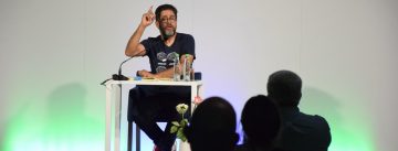Hasnain Kazim sitzend auf dem Podium vor Silhouette des Publikums