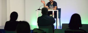 Hasnain Kazim sitzend auf dem Podium vor Silhouette des Publikums