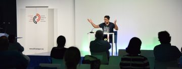 Hasnain Kazim sitzend auf dem Podium vor Silhouette des Publikums