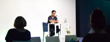 Hasnain Kazim sitzend auf dem Podium vor Silhouette des Publikums