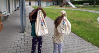 zwei Kinder halten Jutebeutel vor ihren Gesichtern, Quelle: DTF