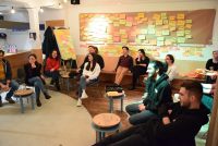 Workshopteilnehmende sitzen auf Stühlen verteilt in einem Raum vor einer Wand mit bunten Zetteln, Quelle: DTF