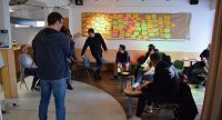 Blick in einen Workshopraum mit Teilnehmenden, die vor einer Wand mit bunten Zetteln sitzen, Quelle: DTF