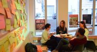 vier Workshopteilnehmende sitzen um einen Tisch vor einer Wand mit bunten Zetteln, Quelle: DTF