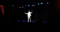 Mann in grauem Anzug spricht gestikulierend auf der Bühne vor Silhouette des Publikums, Quelle: DTF