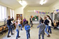 Eine Gruppe Kinder und junger Frauen stehen im Kreis in einem Klassenzimmer und tanzen, Quelle: DTF