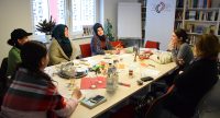 Frauen mit und ohne Kopftuch sitzen um einen Konferenztisch und unterhalten sich, Quelle: DTF