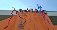 fröhliche Kinder mit bunten Stoffbändern auf einem orangenen Balkon., Quelle: DTF