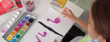 Tisch auf dem Kinder gerade mit Wasserfarben Flamingos malen (von oben fotografiert)