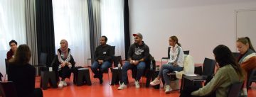 Workshopteilnehmende sitzen in einem Halbkreis und hören einer Moderatorin zu